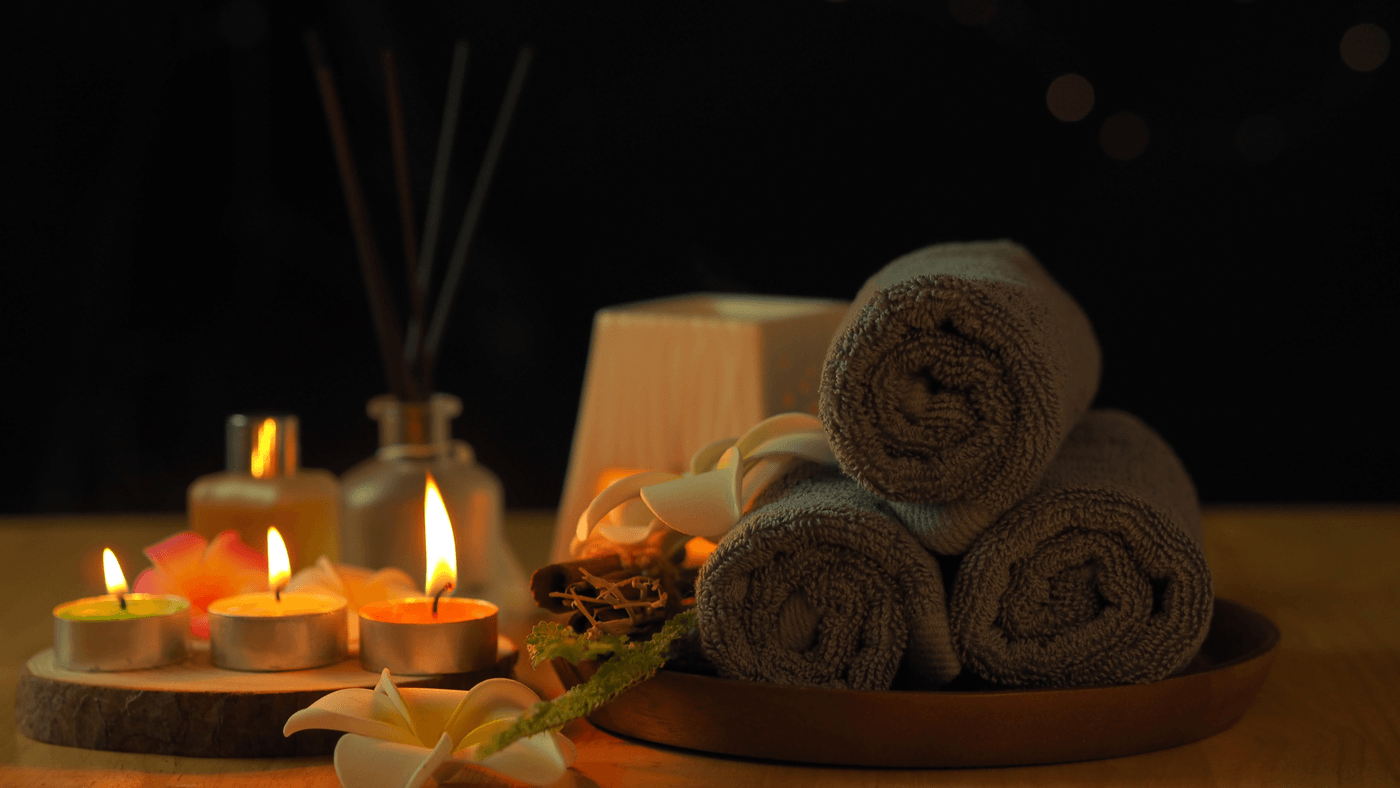 Rolled spa towels, lit candles, and frangipani flowers by candlelight